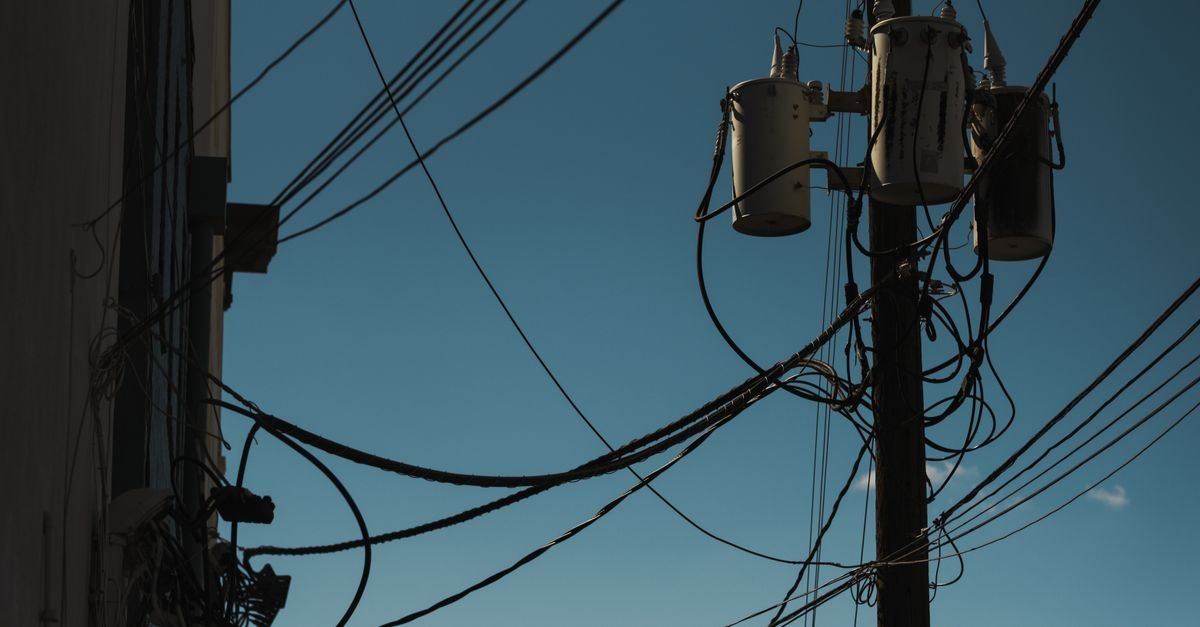 Poste de energia com transformadores e emaranhado de cabos contra o céu azul