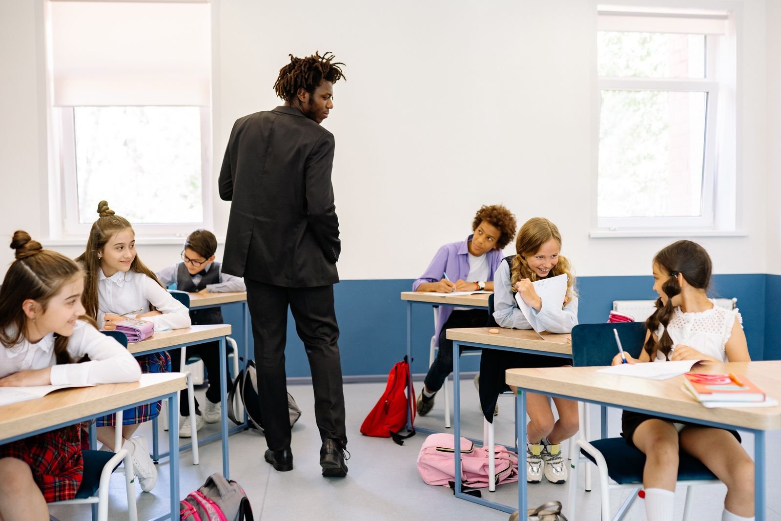 Professor de pé em sala de aula conversa com alunos sentados nas carteiras (imagem ilustrativa)