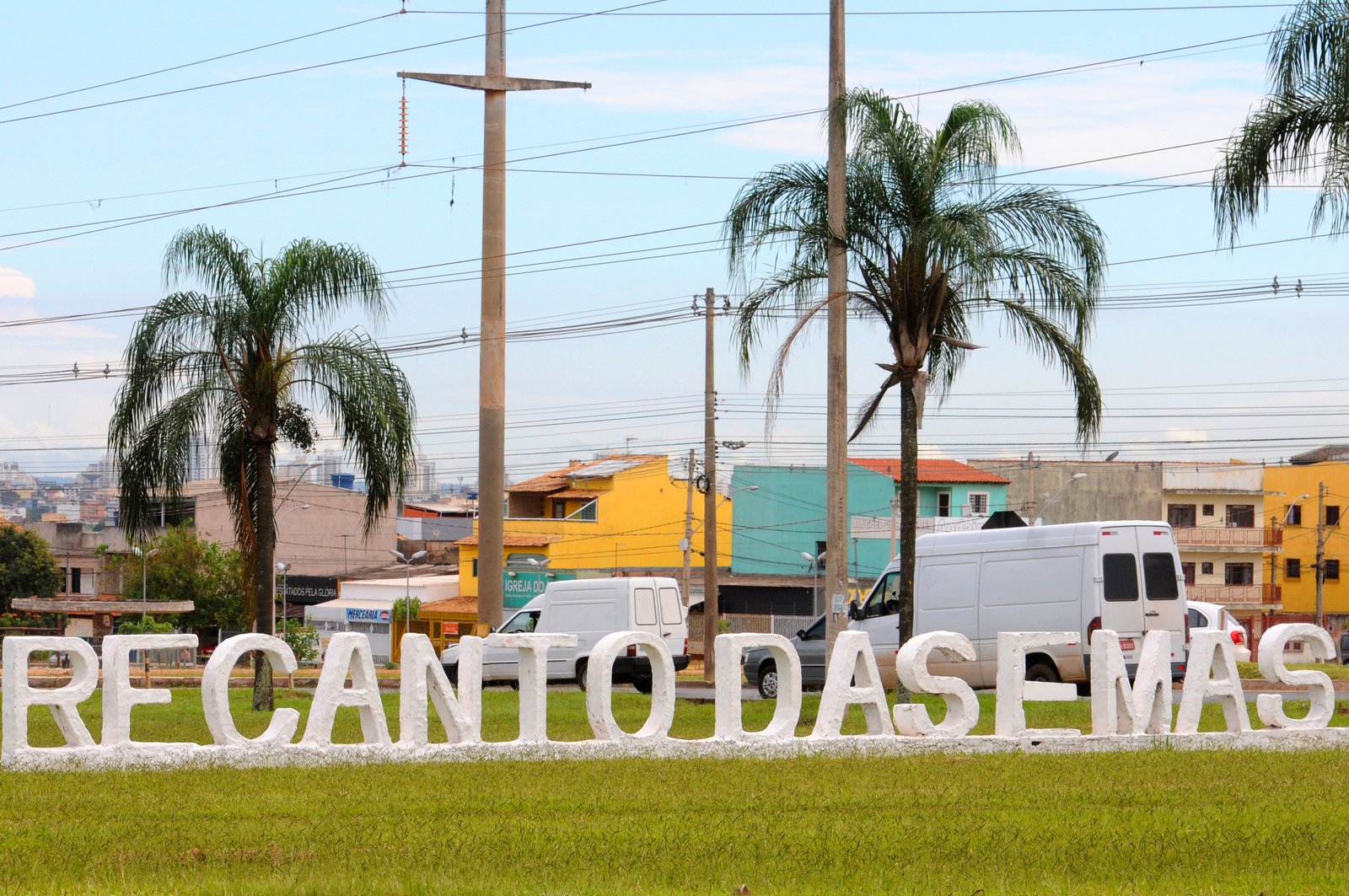 Letreiro com o nome Recanto das Emas em frente a casas e palmeiras da região administrativa