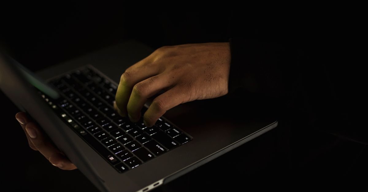 Mãos digitando em teclado de notebook em ambiente escuro