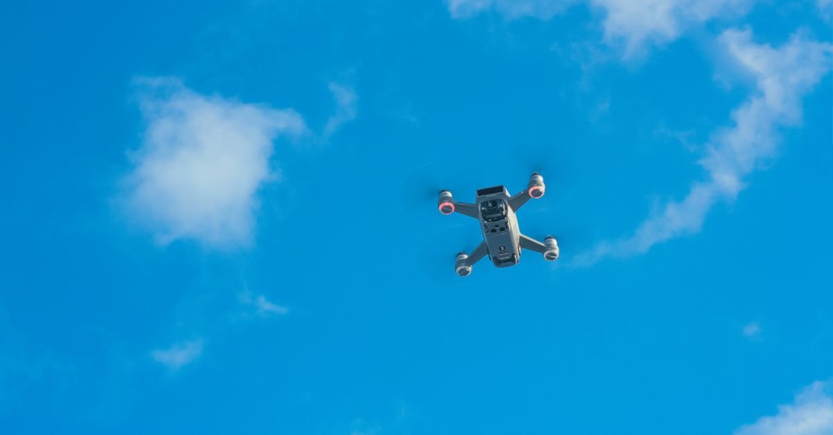 Drone quadricóptero visto de baixo, em voo contra o céu azul com nuvens