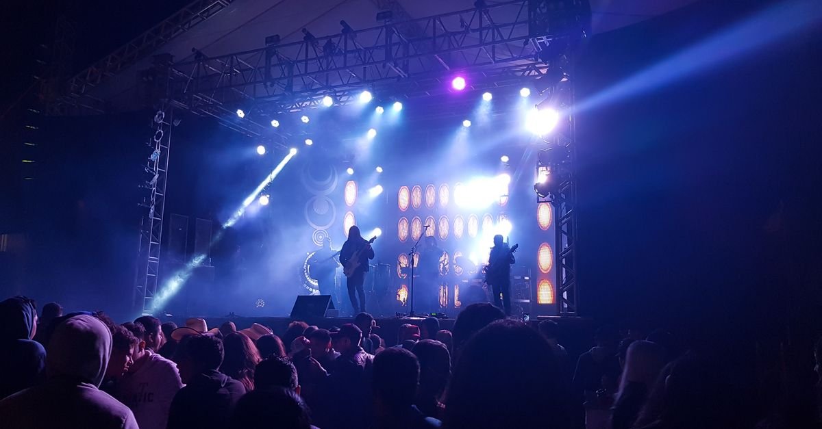 Palco de festival de música iluminado com público em silhueta durante show noturno