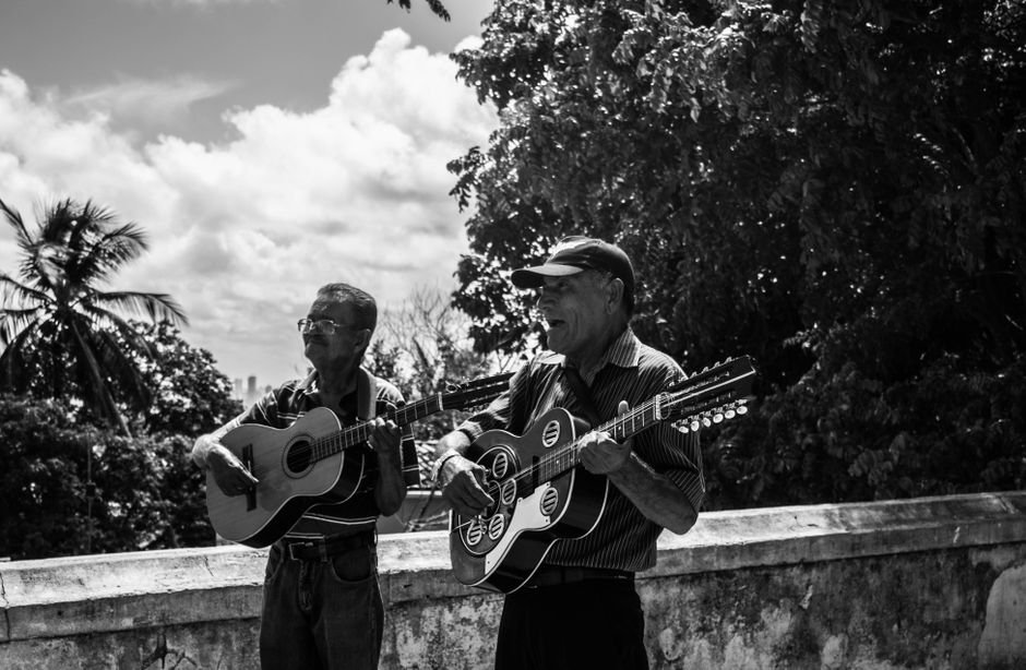 Dois músicos tocam violão e cantam ao ar livre em registro em preto e branco