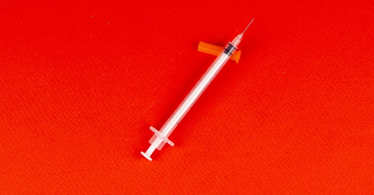 Seringa descartável sobre fundo vermelho, em imagem que ilustra campanha de vacinação