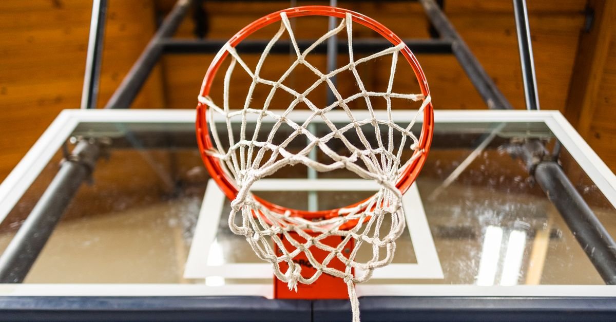 Cesta de basquete vista de baixo, com rede branca e tabela de vidro em ginásio coberto