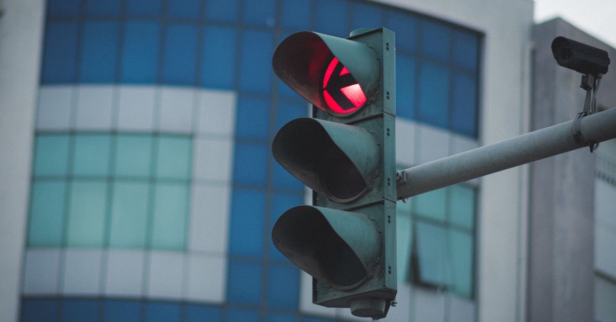 Semáforo com luz vermelha acesa em cruzamento urbano, com prédio ao fundo