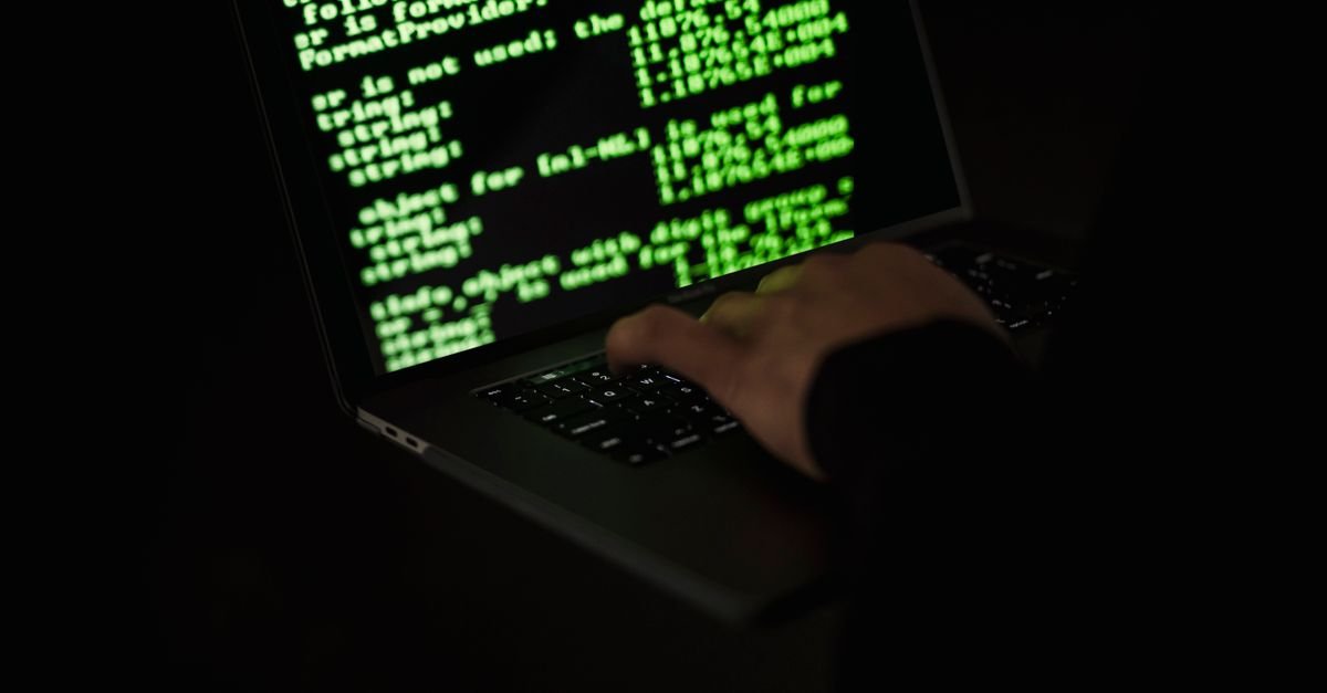 Mão sobre teclado de notebook com código na tela em ambiente escuro