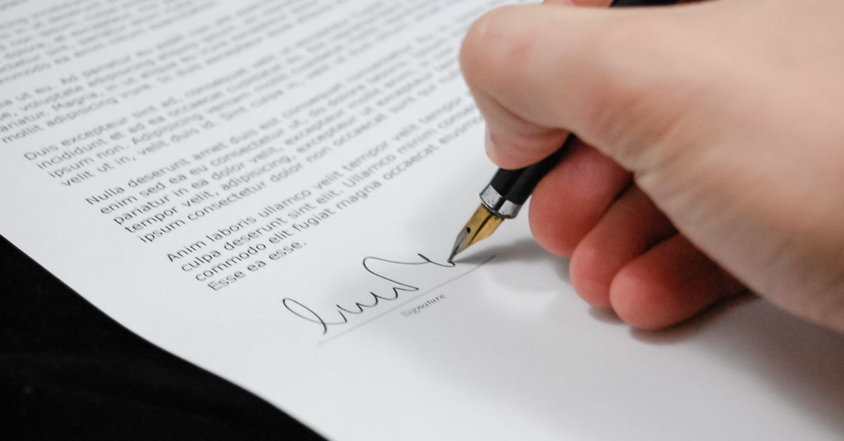 Mão segurando caneta-tinteiro ao assinar a linha de assinatura de um documento impresso