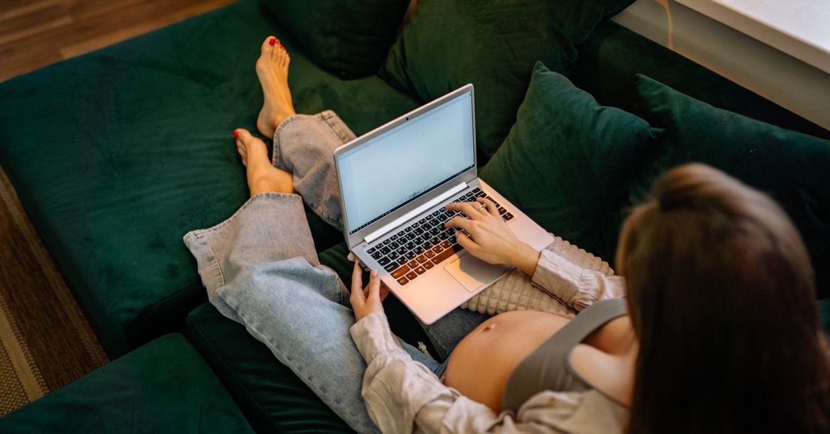 Mulher grávida sentada em sofá trabalhando em notebook