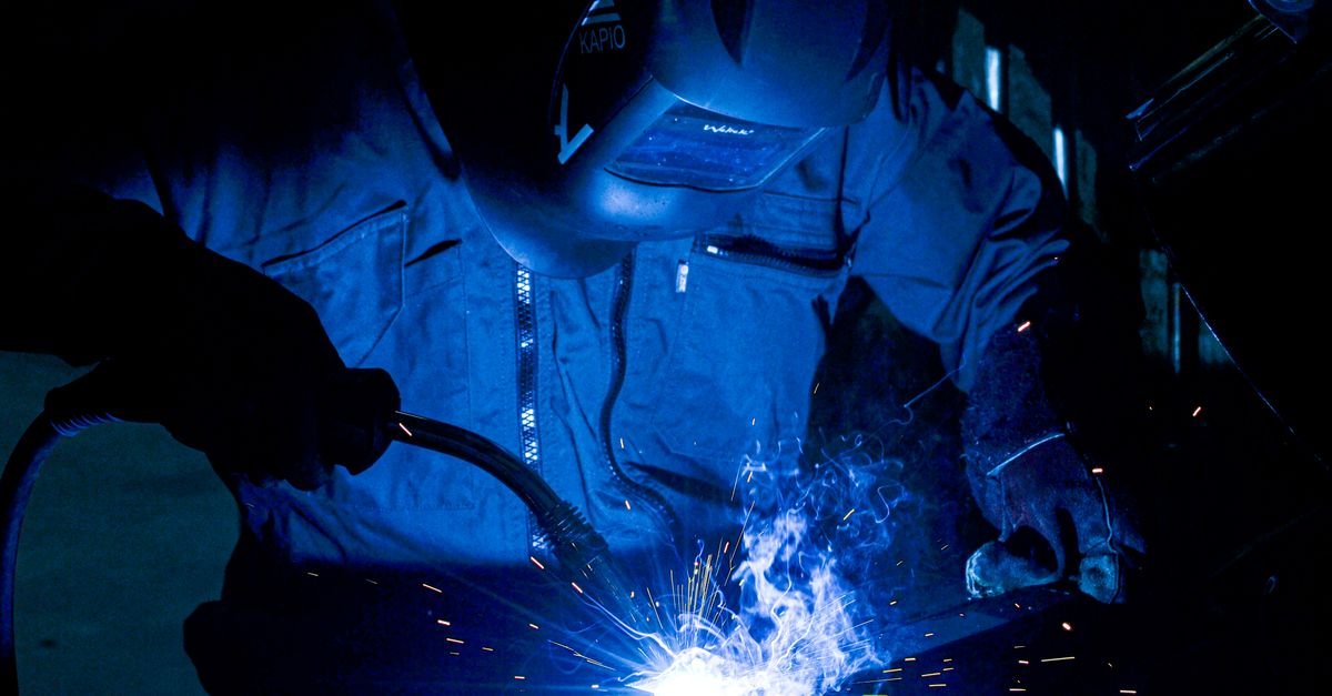Soldador com máscara de proteção trabalha com faíscas em oficina industrial