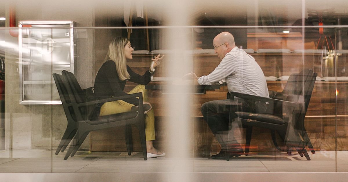 Dois profissionais conversam sentados em escritório moderno