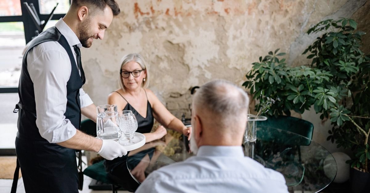 Garçom serve bebidas a clientes sentados à mesa de um restaurante