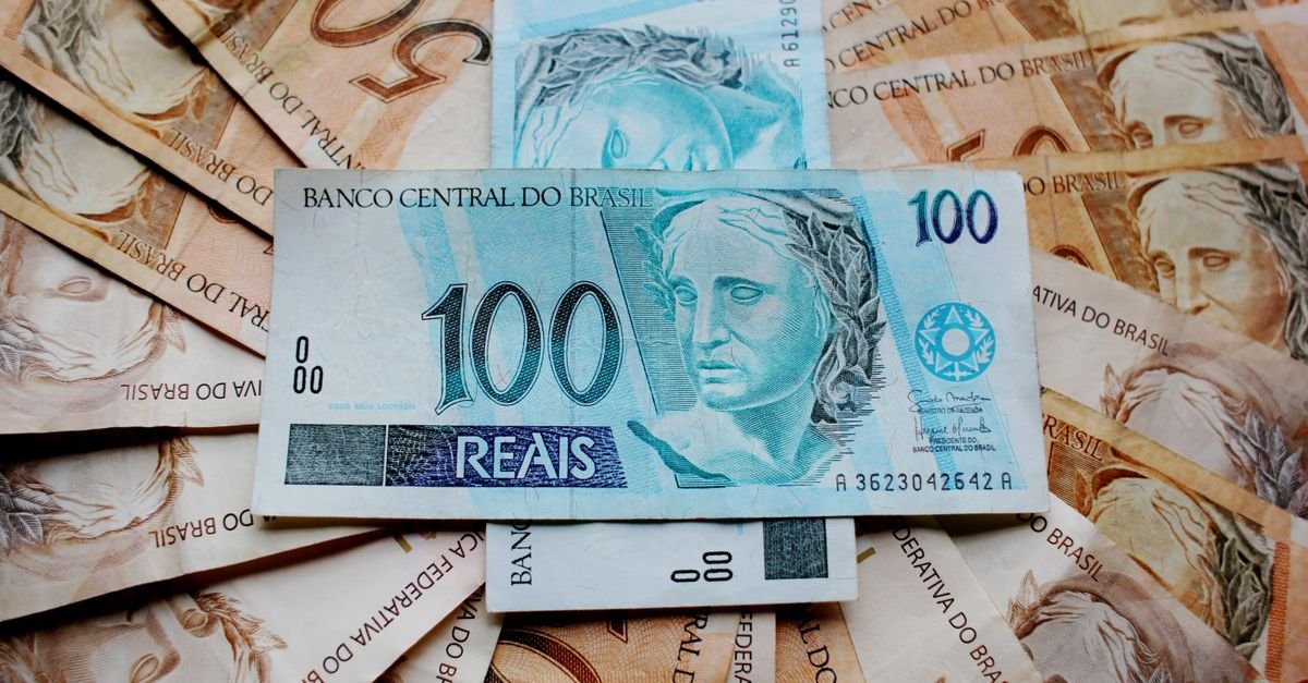Notas de real espalhadas sobre uma mesa, com cédula de cem reais em destaque