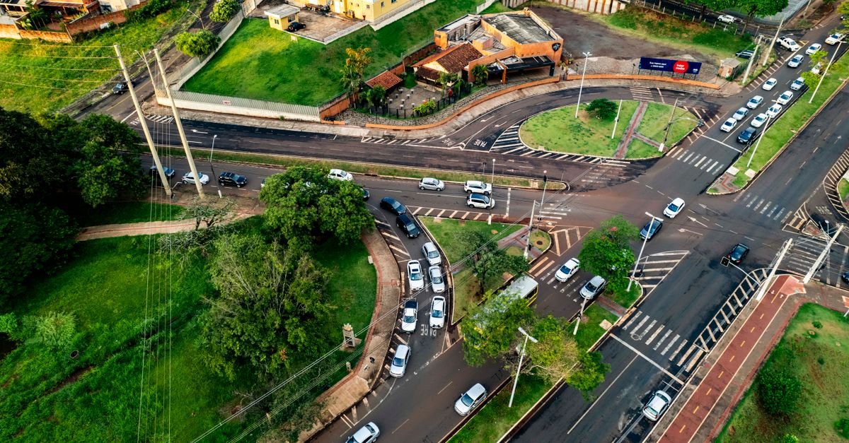 Vista aérea de cruzamento urbano brasileiro com carros parados e faixa de pedestres