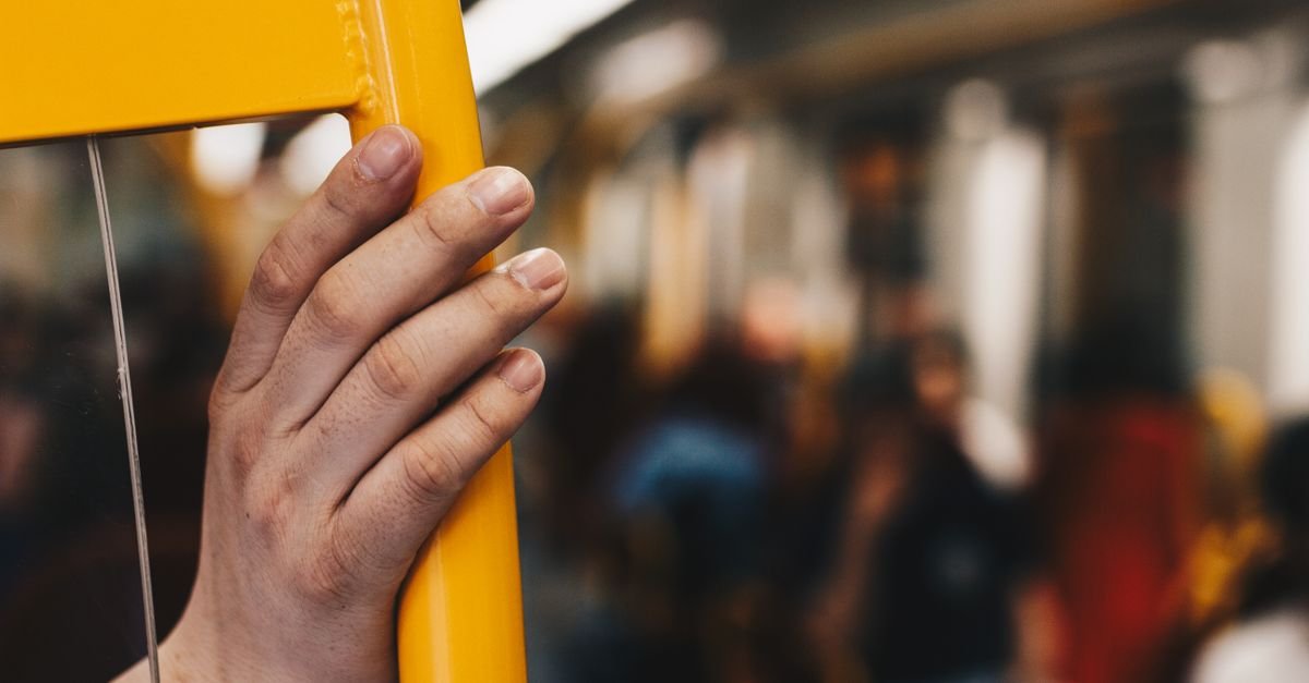 Mão de passageiro segurando corrimão amarelo dentro de transporte público