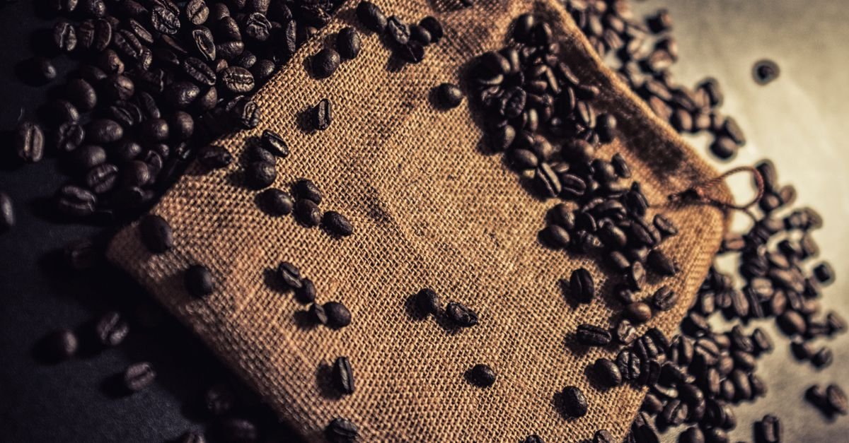 Grãos de café torrado espalhados sobre saco de estopa