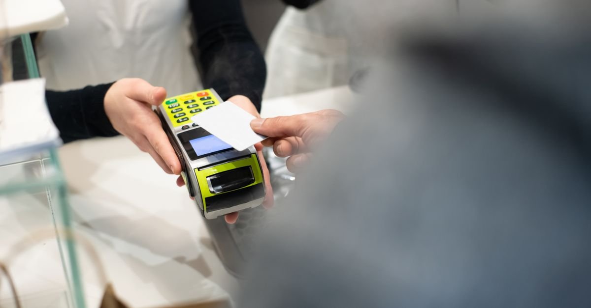 Cliente aproxima cartão de pagamento de maquininha em balcão de loja