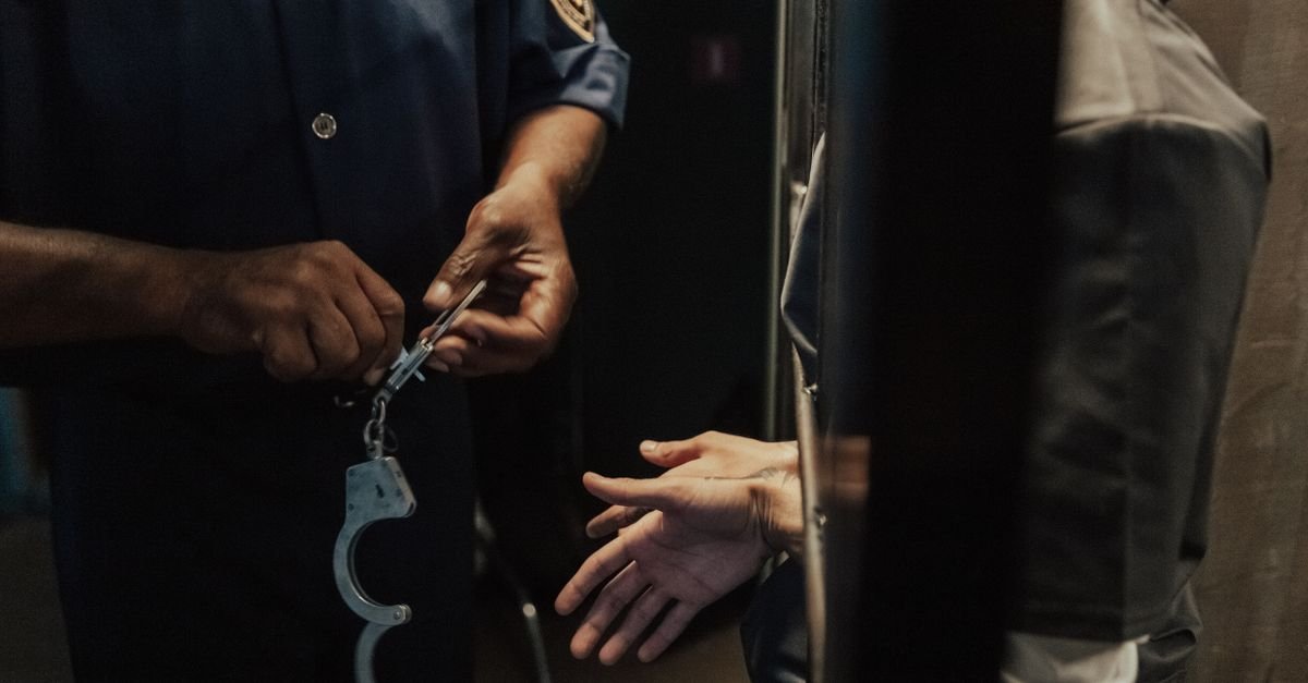 Mãos de um policial segurando algemas metálicas durante uma detenção