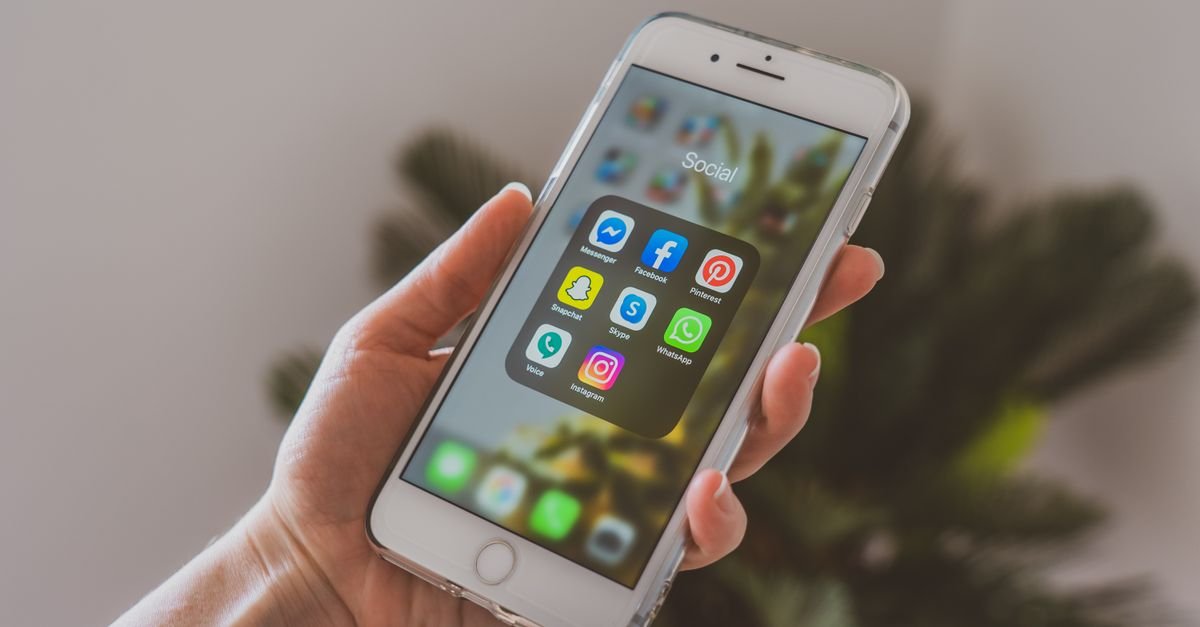 Mão segura celular com pasta de aplicativos de redes sociais aberta na tela