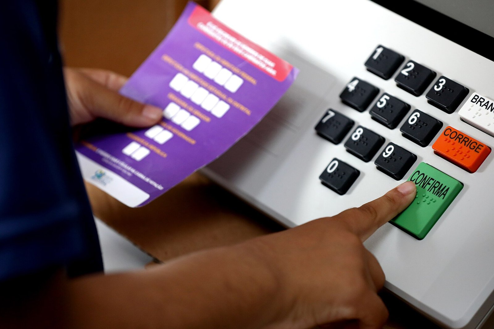 Mão de estudante pressiona a tecla confirma de uma urna eletrônica