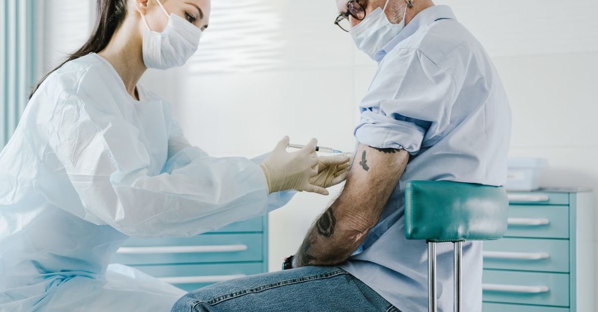 Profissional de saúde aplica vacina no braço de um homem em consultório