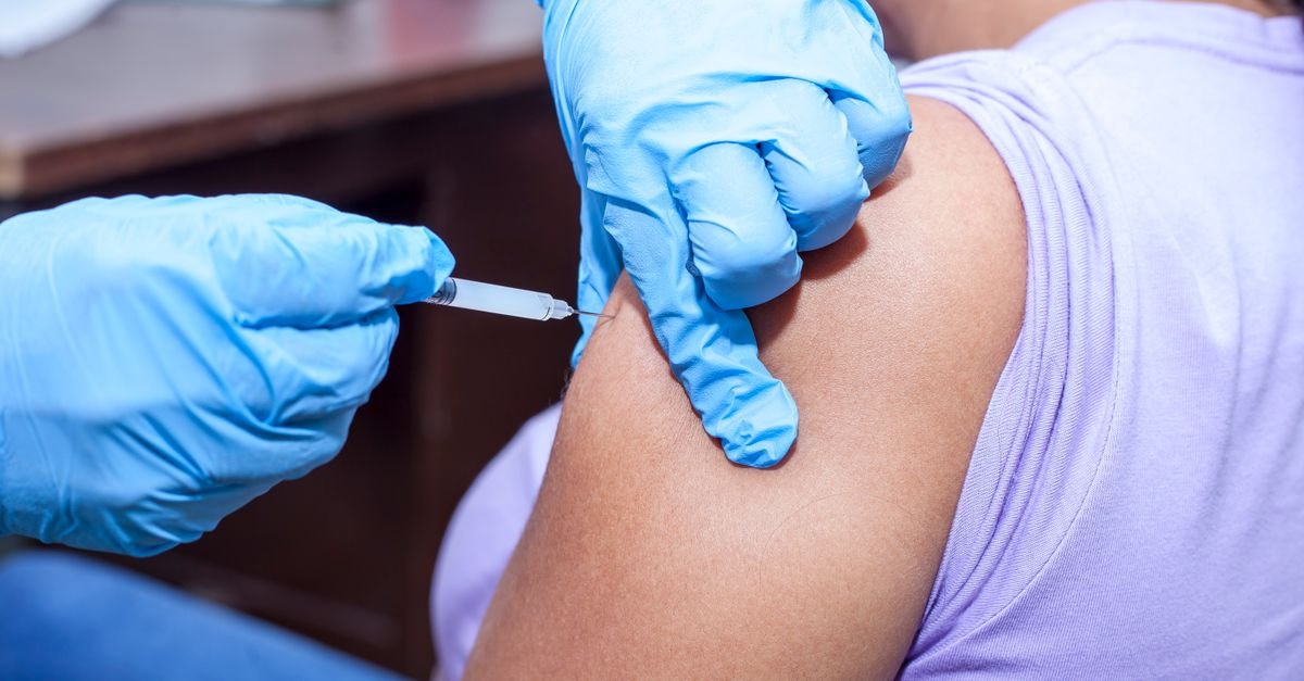 Profissional de saúde com luvas azuis aplica vacina no braço de um paciente