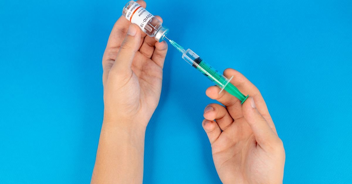 Mãos preparando dose de vacina com seringa e frasco sobre fundo azul