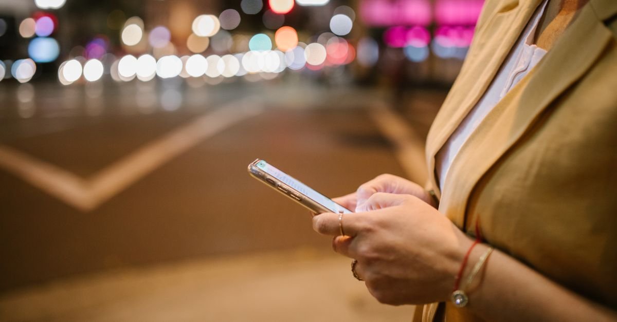 Mãos de uma mulher segurando um celular em rua movimentada à noite